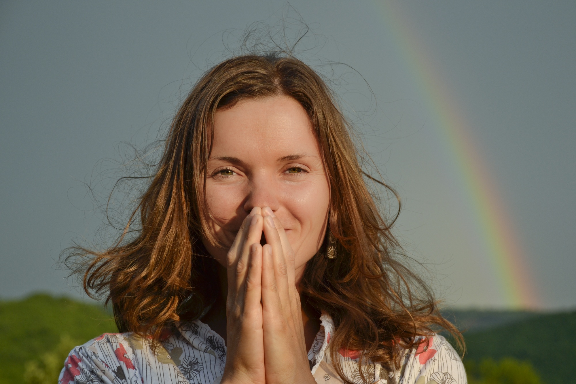 gratitude in small things: woman smiling with prayer hands in front of her face and a rainbow in the background