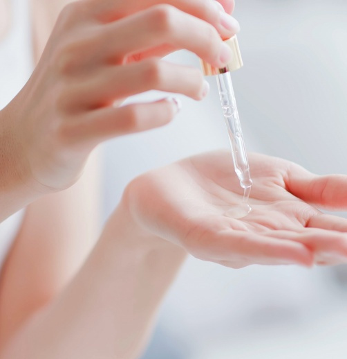 Layering skin care products woman applying serum in palm of hand using a dropper