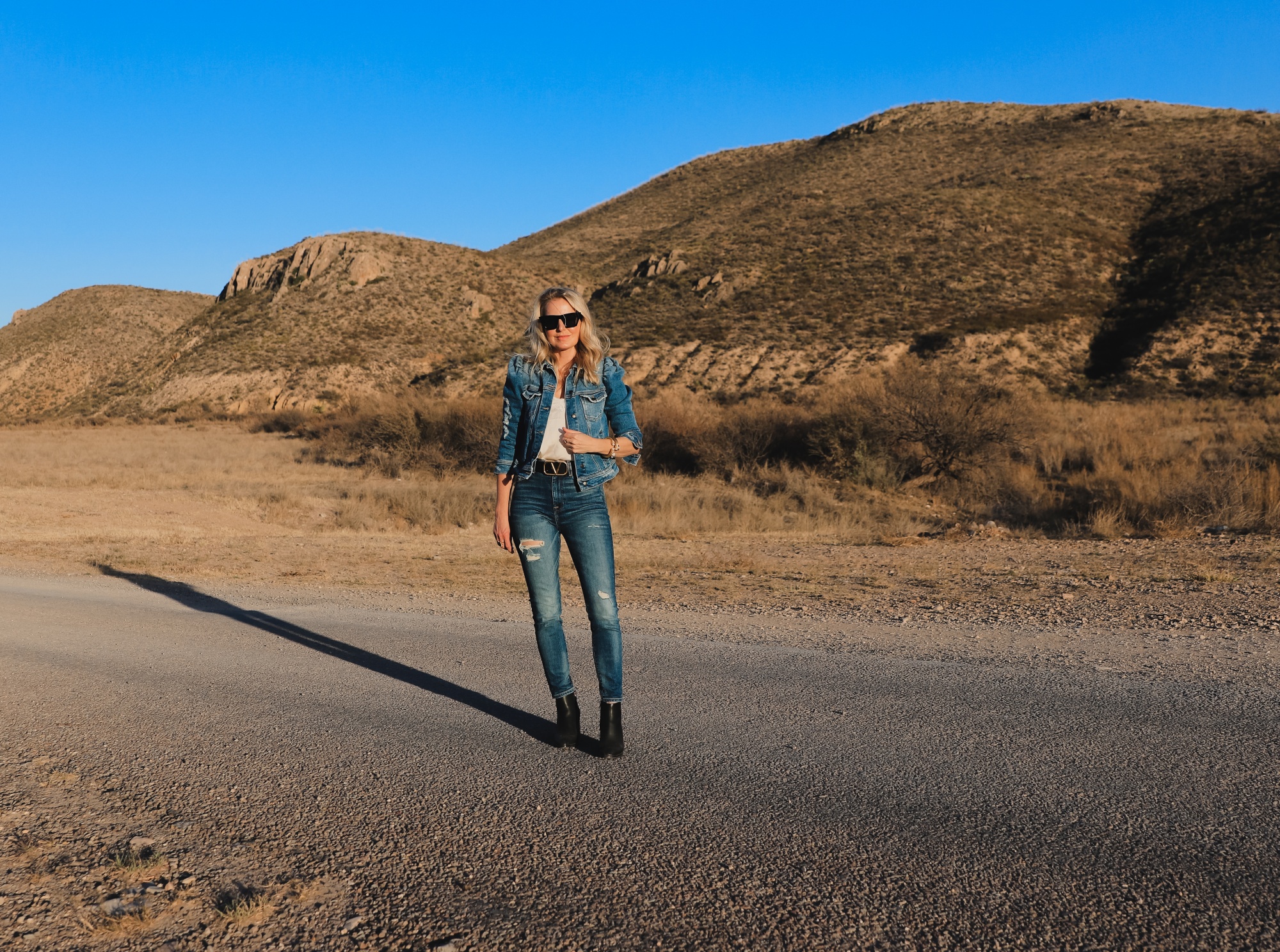How To Wear Denim on Denim, Erin Busbee of Busbee wearing a distressed puff sleeve denim jacket by Retrofete, 7 For All Mankind distressed jeans, black Alexander Wang cutout booties, white B.P. lace cami, black cat eye sunglasses, and Julie Vos gold cuff bracelets in West Texas