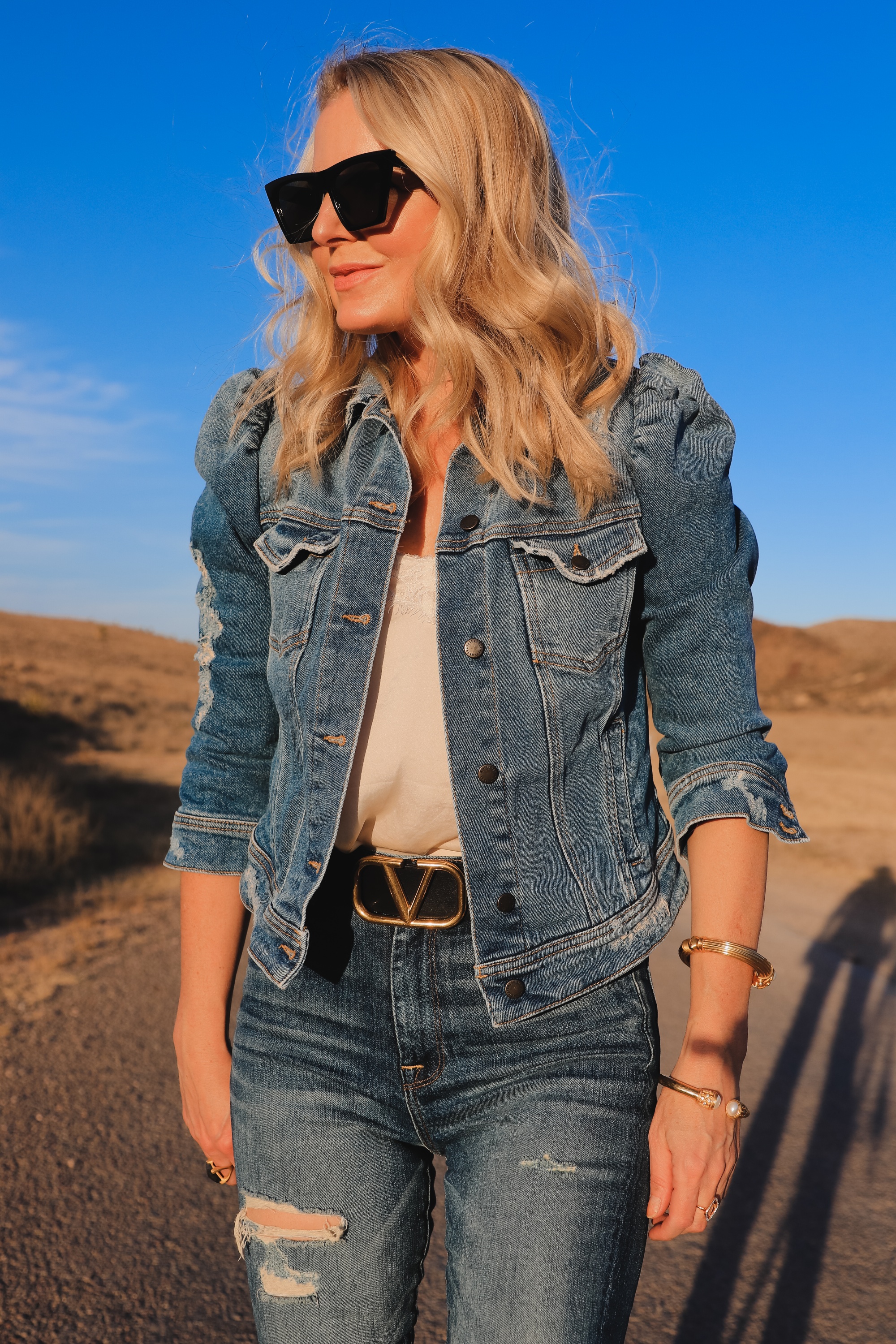 How To Wear Denim on Denim, Erin Busbee of Busbee wearing a distressed puff sleeve denim jacket by Retrofete, 7 For All Mankind distressed jeans, black Alexander Wang cutout booties, white B.P. lace cami, black cat eye sunglasses, and Julie Vos gold cuff bracelets in West Texas