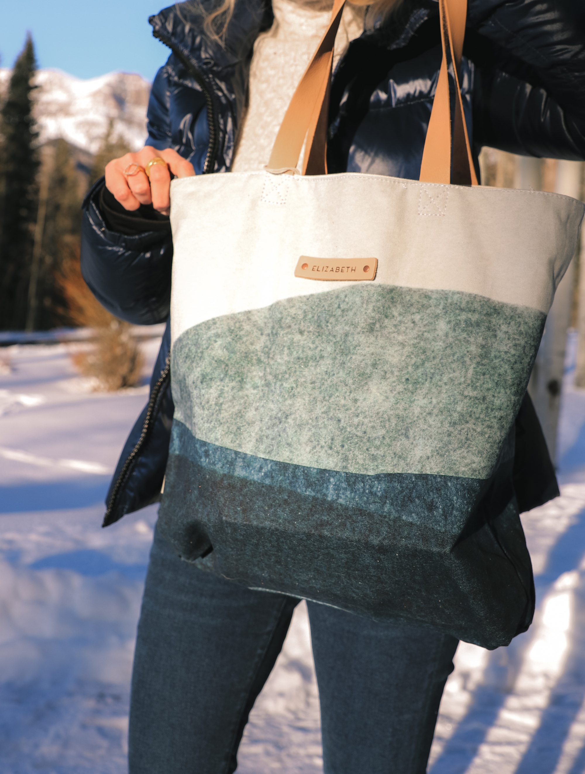 Personalized Gifts, Erin Busbee of Busbee Style carrying a blue and white personalized tote bag from Minted wearing a SAM. puffer jacket with a cable knit sweater and jeans in Telluride, Colorado