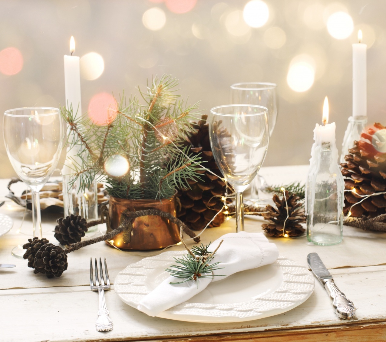 Hostess gifts that aren't boring showing a holiday table scape with pinecones, candles and dinner ware