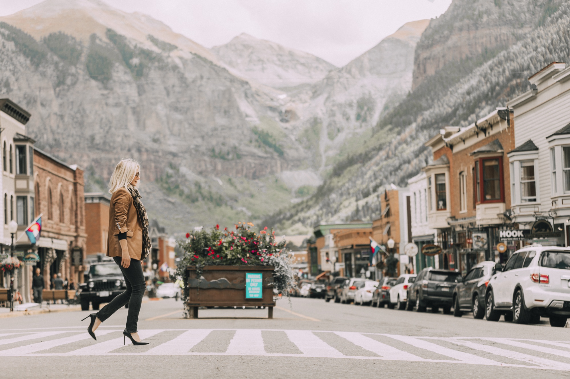 blonde fashion over 40 blogger Erin Busbee crossing main street in Downtown Telluride, Colorado wearing tan leather blazer, black skinny jeans and leopard pumps