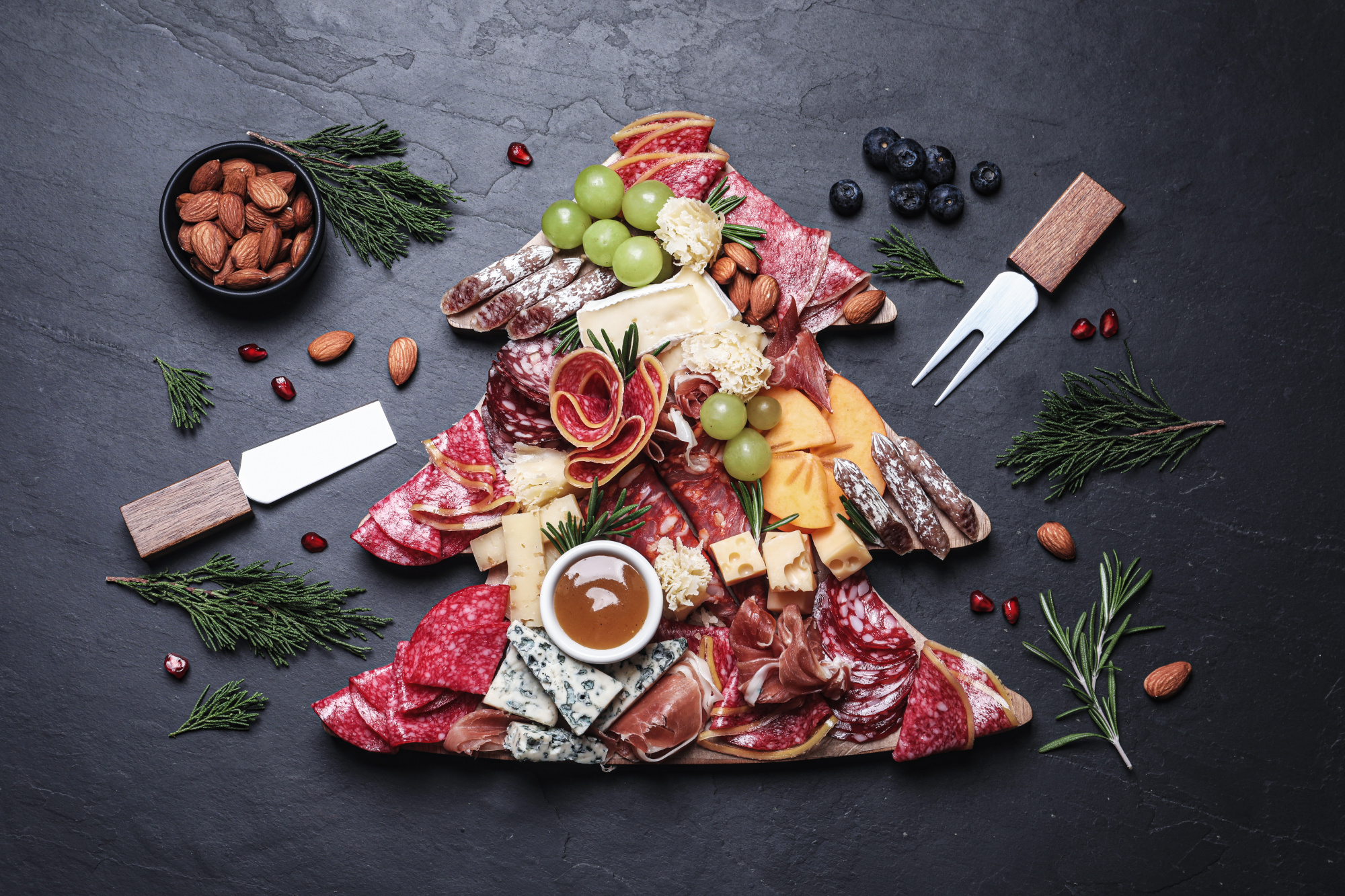 charcuterie board shaped as Christmas tree, Fir tree shaped board with different appetizers and sauce on black table, appetizers for the Holidays, how to make a charcuterie board, cheese board