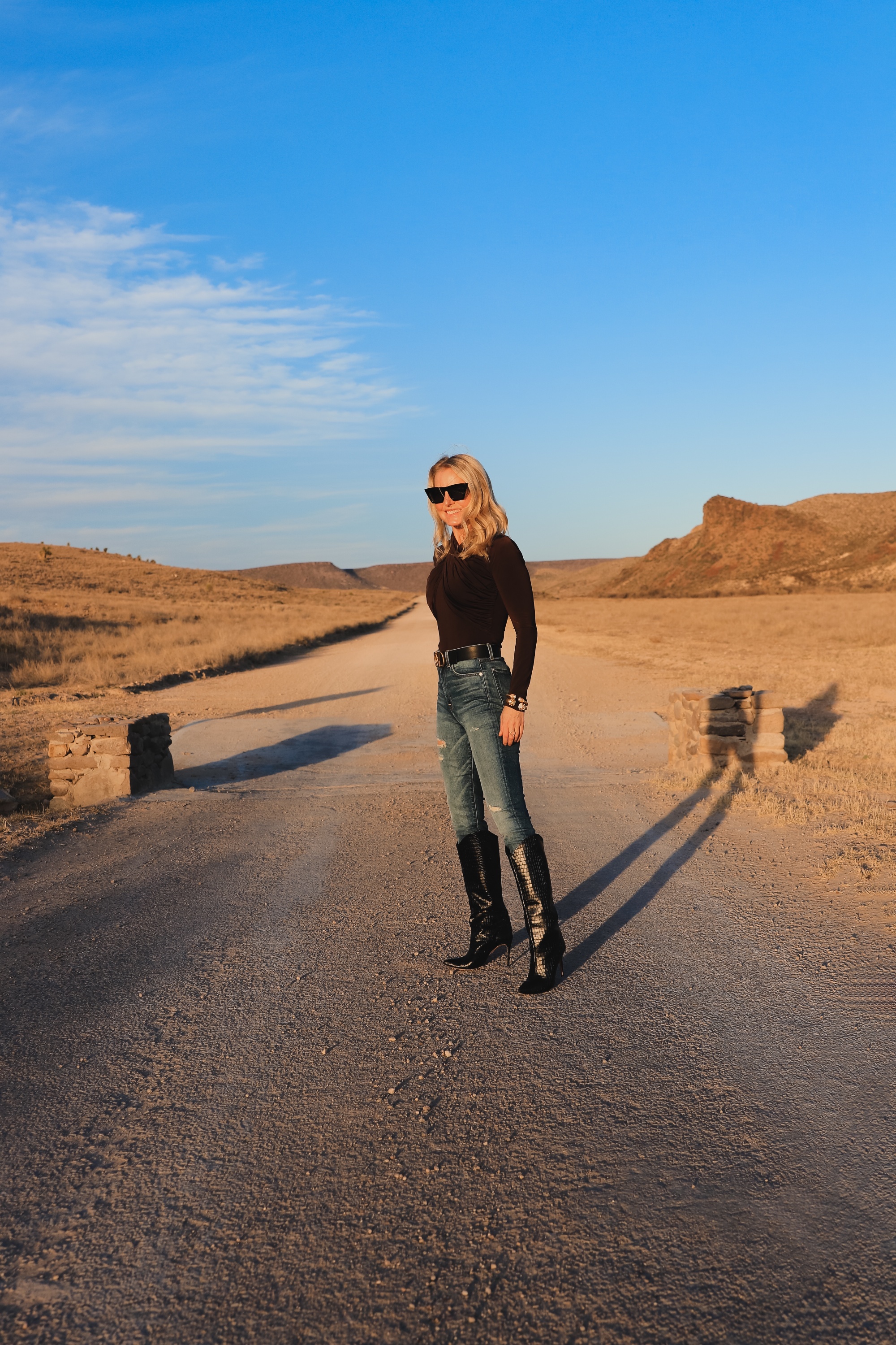 Brown and black outfit, Erin Busbee of Busbee Style wearing a dark brown wrapped neck top by Lovers + Friends tucked into 7 for all mankind ripped jeans with black snake-embossed knee-high boots and black reversible Valentino belt in west Texas