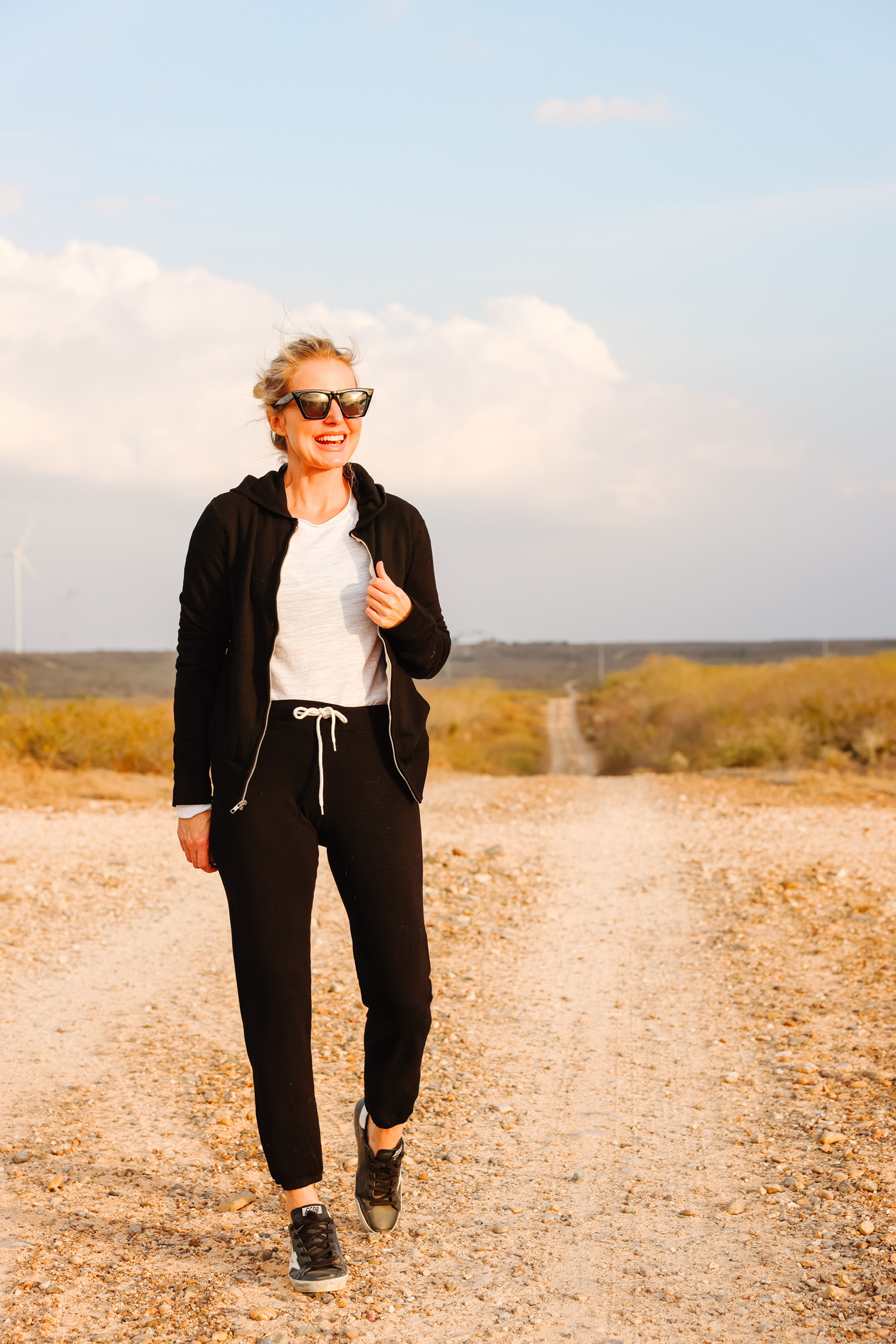 Cozy Loungewear, Erin Busbee of Busbee wearing a black hoodie by Monrow over a white long sleeve tee by Free People tucked into black drawstring joggers by Monrow and black Golden Goose sneakers walking on their ranch in south Texas