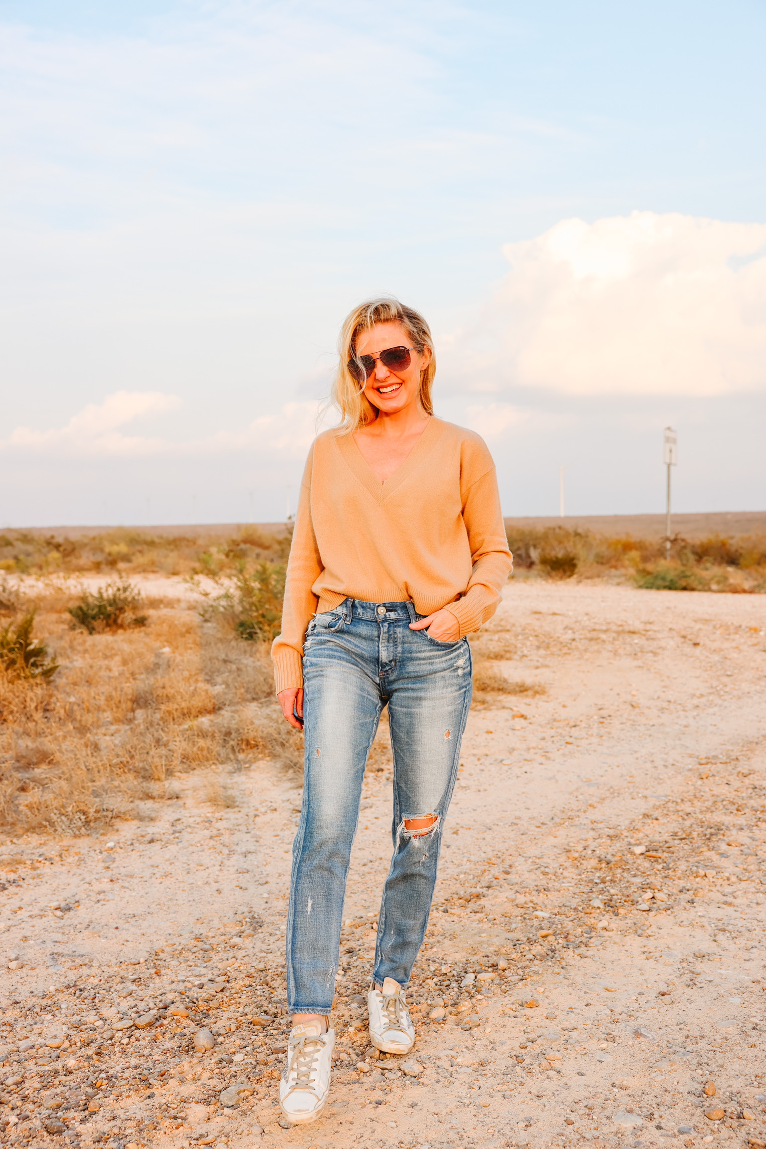 elevated basics, Erin Busbee of Busbee wearing a camel cashmere v-neck sweater from INtermix with distressed skinny jeans by Moussy Vintage and white golden goose sneakers in south Texas, hottest summer shoes