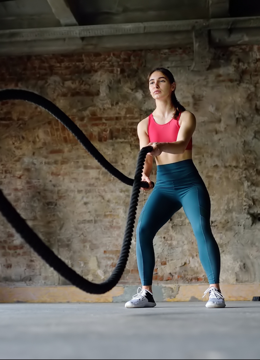 most effective exercise methods for women over 40, long dark-haired woman in bright pink sports bra and teal leggings with battle ropes
