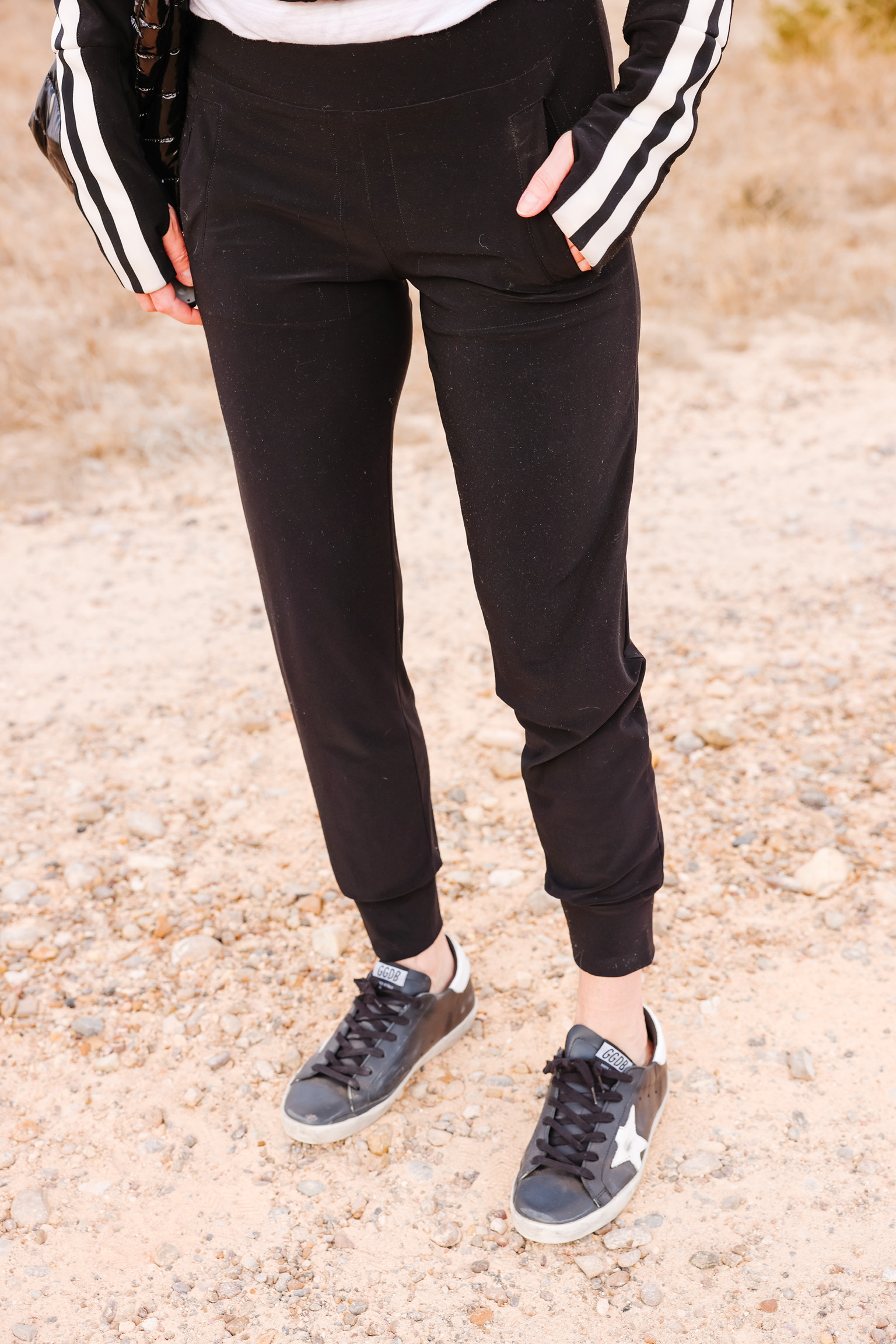 Cozy Loungewear, Erin Busbee of Busbee wearing a black striped Norma Kamali jacket with black norma kamali joggers and black golden goose sneakers carrying a think royln tote in South Texas, Elevated Basics, affordable activewear for women, Erin Busbee of Busbee wearing black golden goose sneakers with black joggers by Norma Kamali in south texas