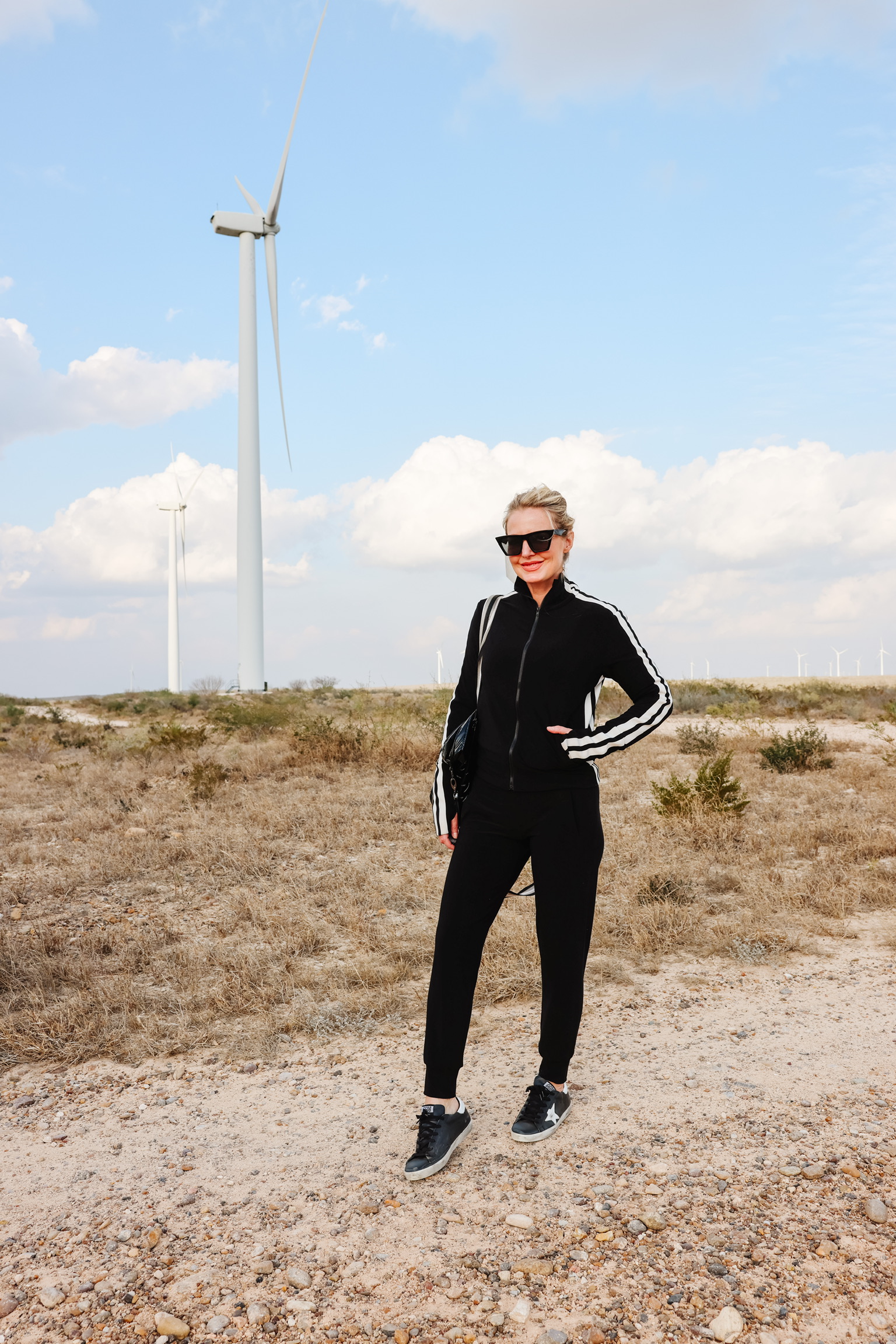Cozy Loungewear, Erin Busbee of Busbee wearing a black striped Norma Kamali jacket with black norma kamali joggers and black golden goose sneakers carrying a think royln tote in South Texas