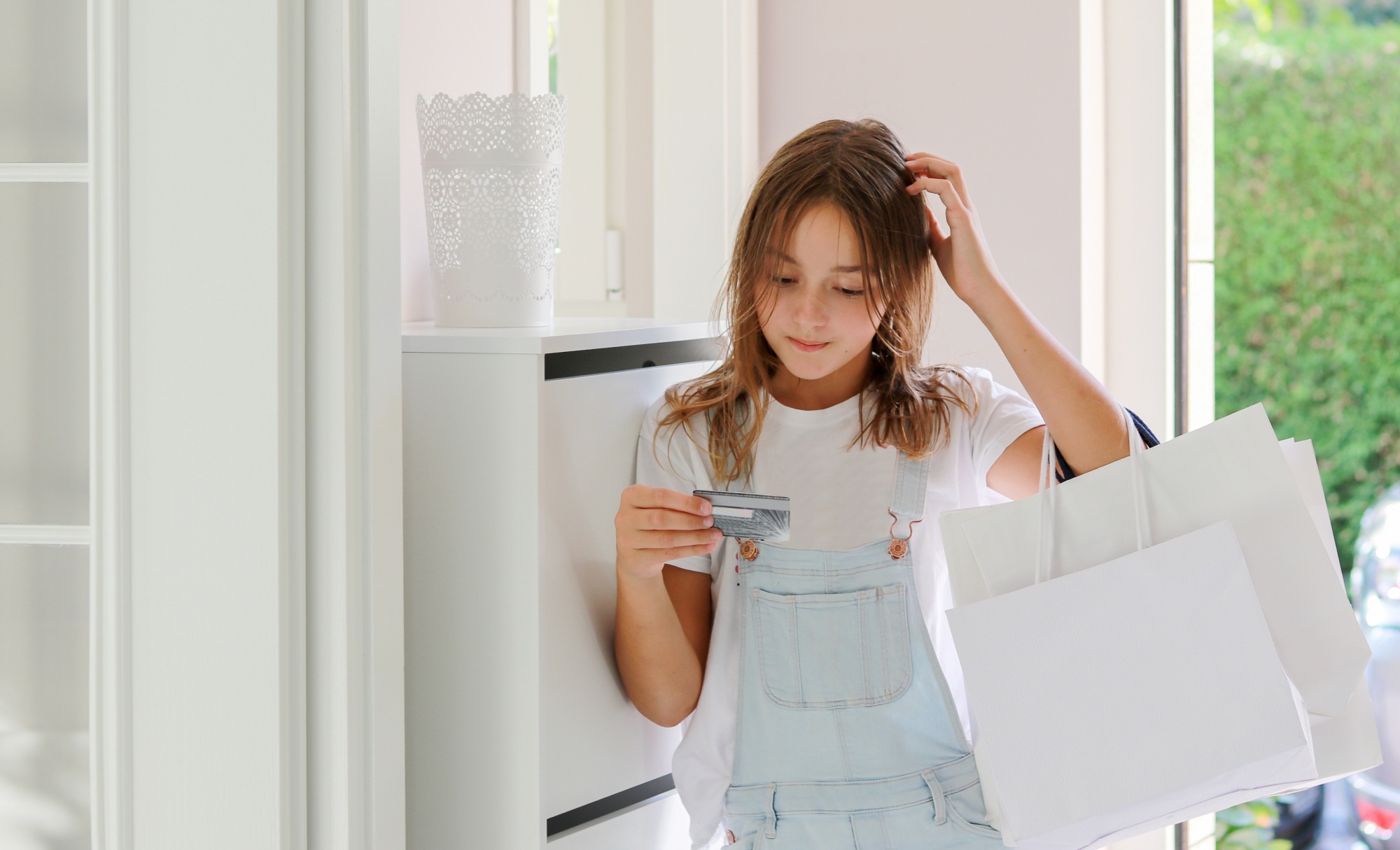 Teaching kids about money, confused tween girl with shopping bags looking at credit card