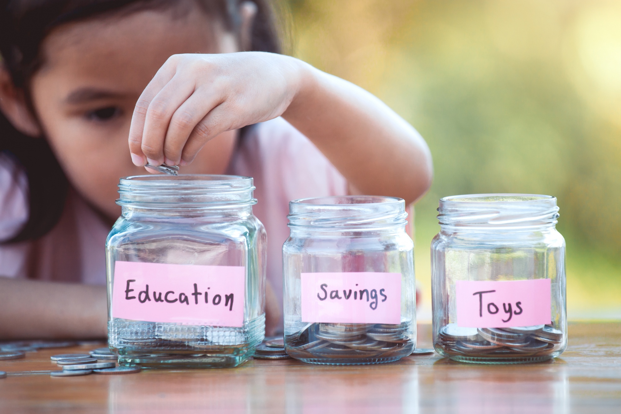 Teaching kids about money, little girl dividing coins into different savings jars