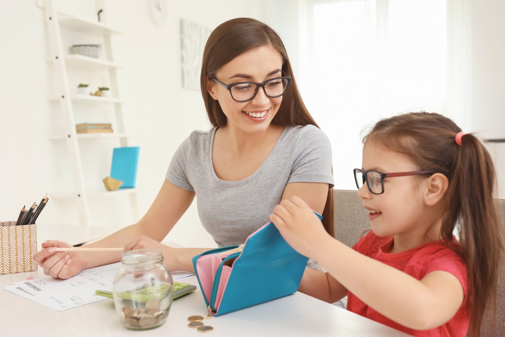 Teaching kids about money, mom and daughter review a budget and money in a wallet together