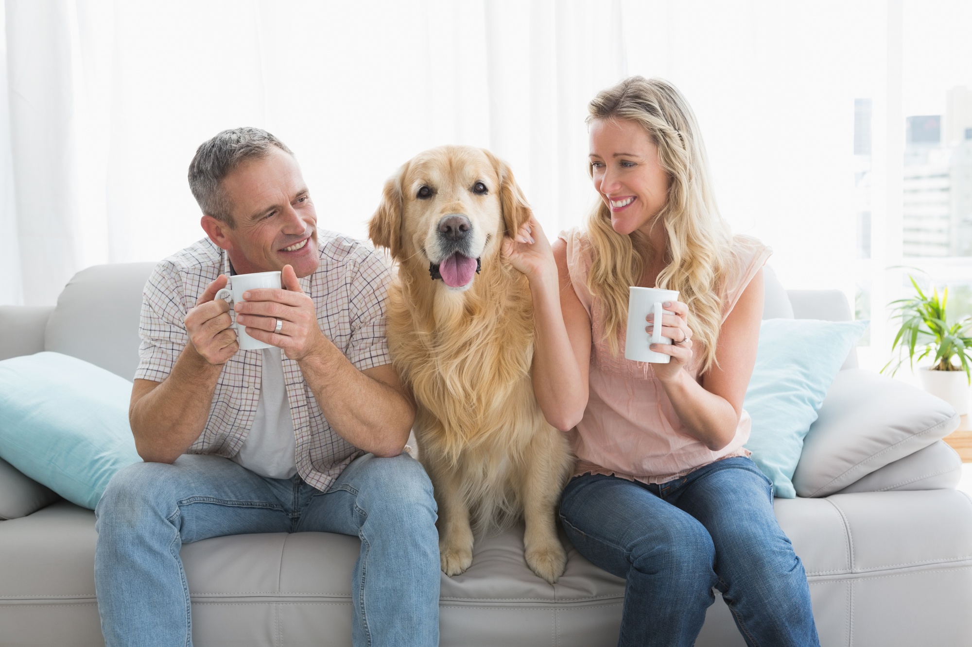 dogs save empty nesters, attractive couple over 40 sitting on the sofa drinking coffee with their golden retriever