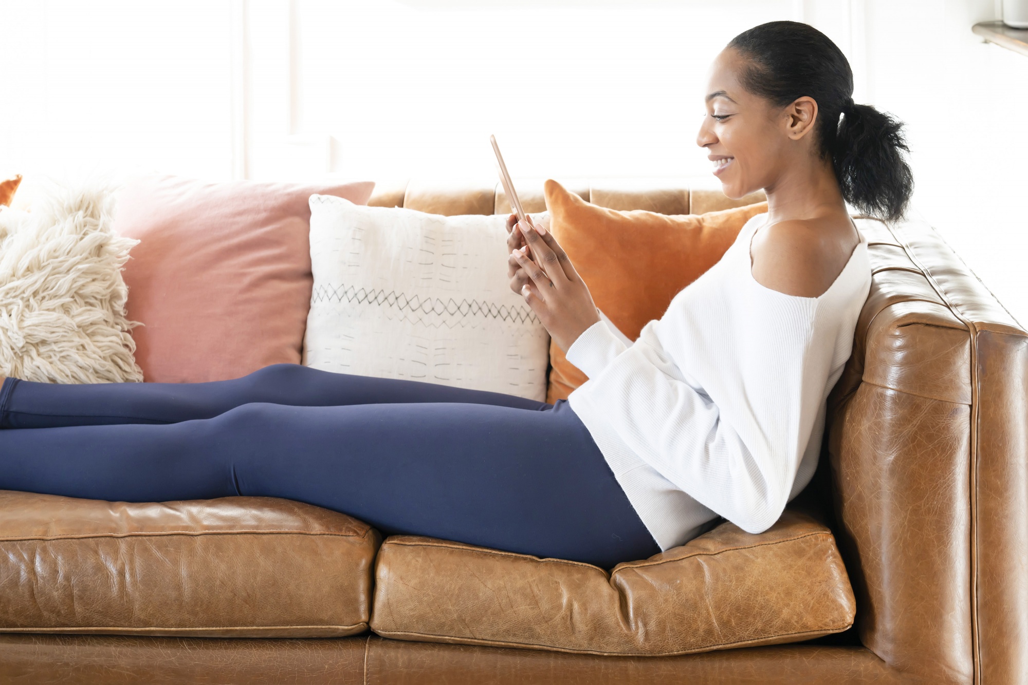 How to Avoid Exercise Injury Over 40, Black woman with ponytail blue leggings white shirt on leather couch reading tablet