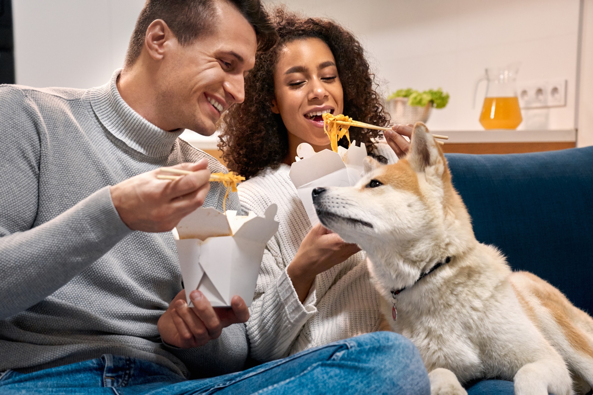 dogs save empty nesters, attractive ethnic couple over 40 sitting on the sofa eating Chinese take-out with their dog