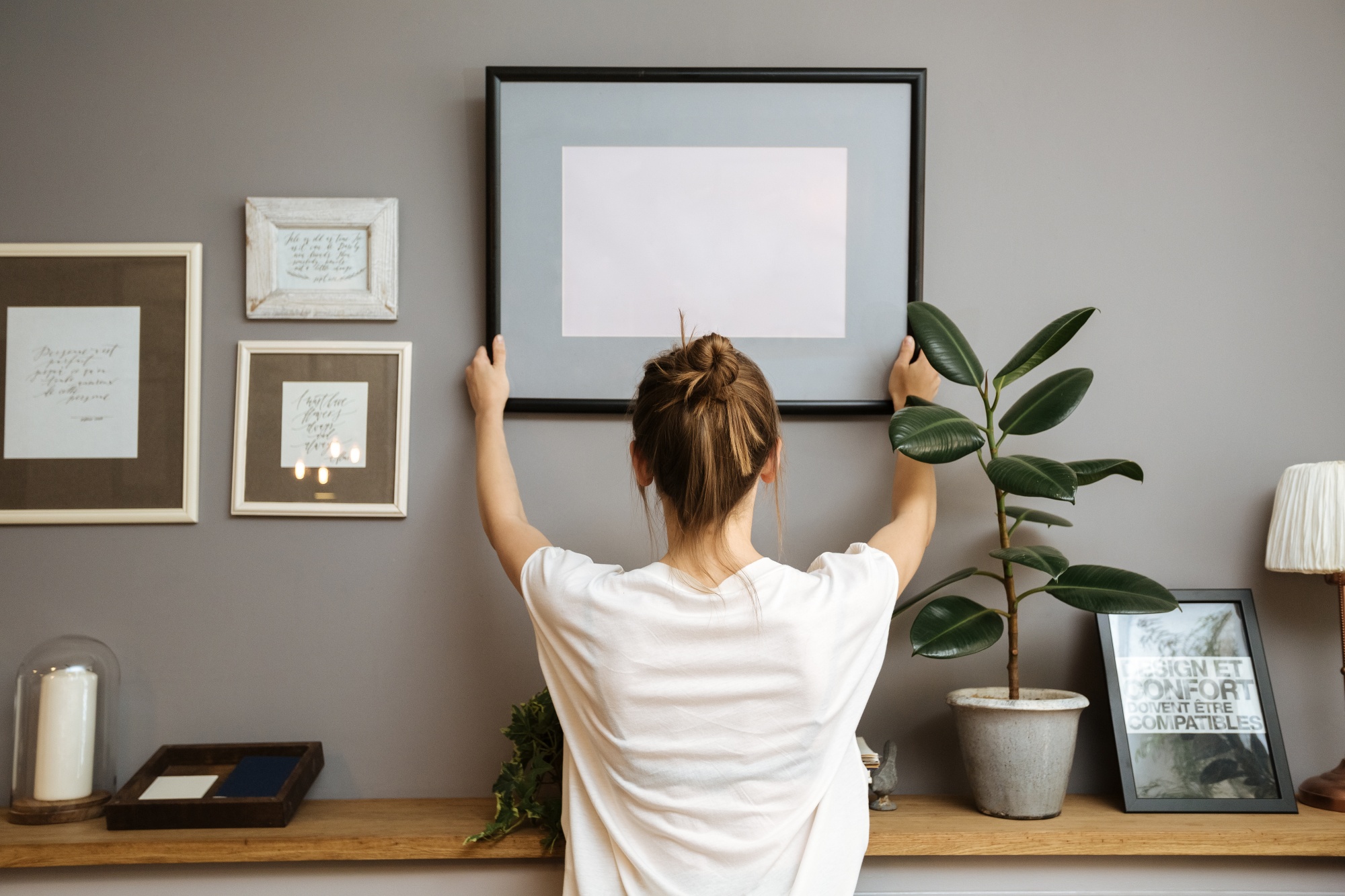  Update Your Home Avoiding 3 Décor Mistakes. Woman hanging wall art above a console table.