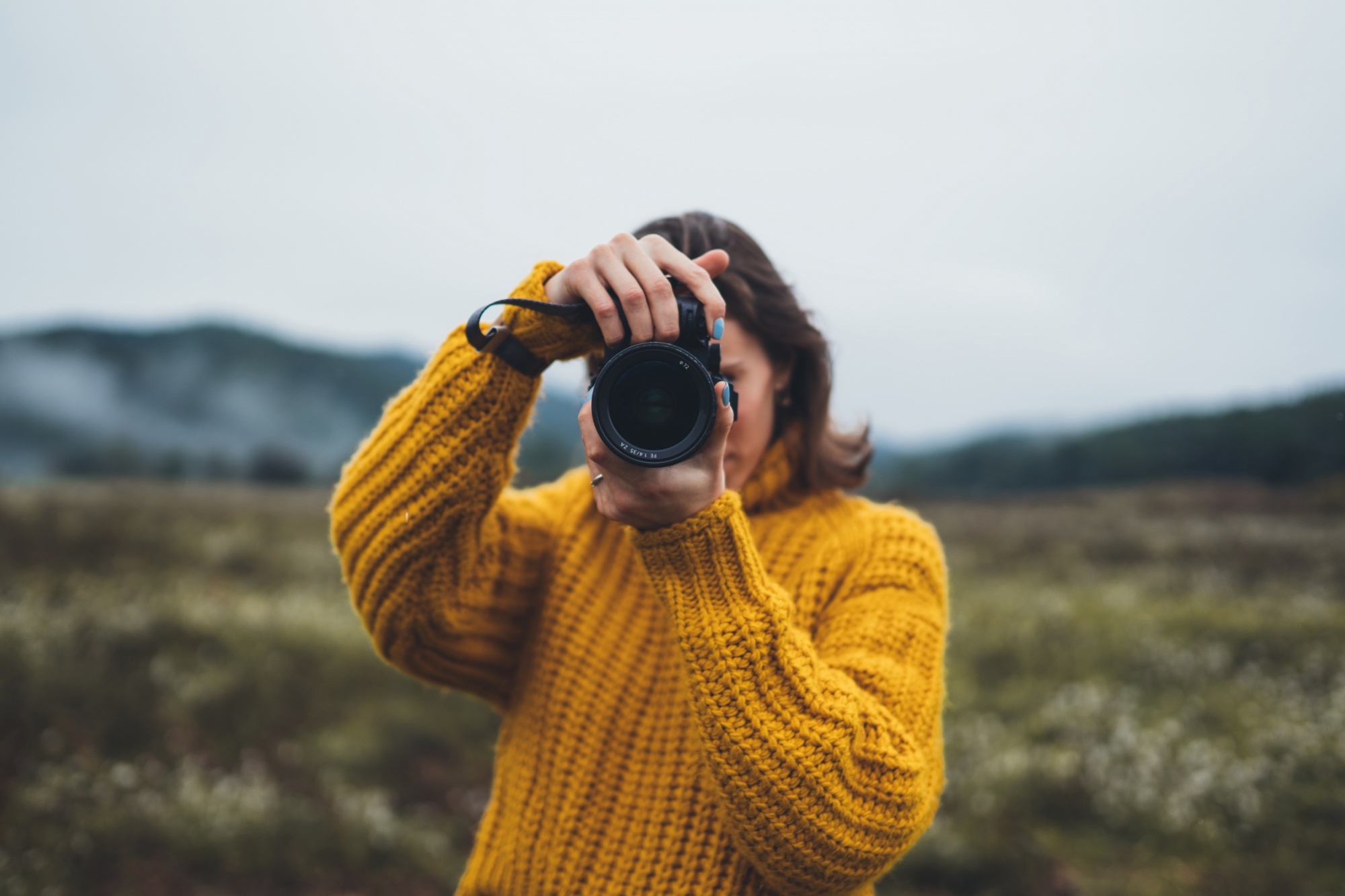 better sex after menopause, Woman in yellow sweater with camera in field with moutain