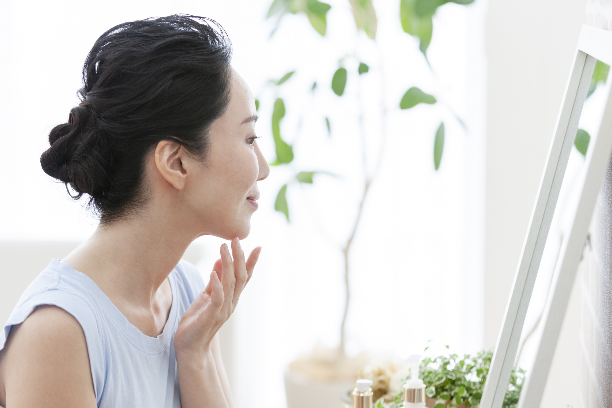 why reinventing yourself makes you younger, Asian woman looking in mirror touching chin