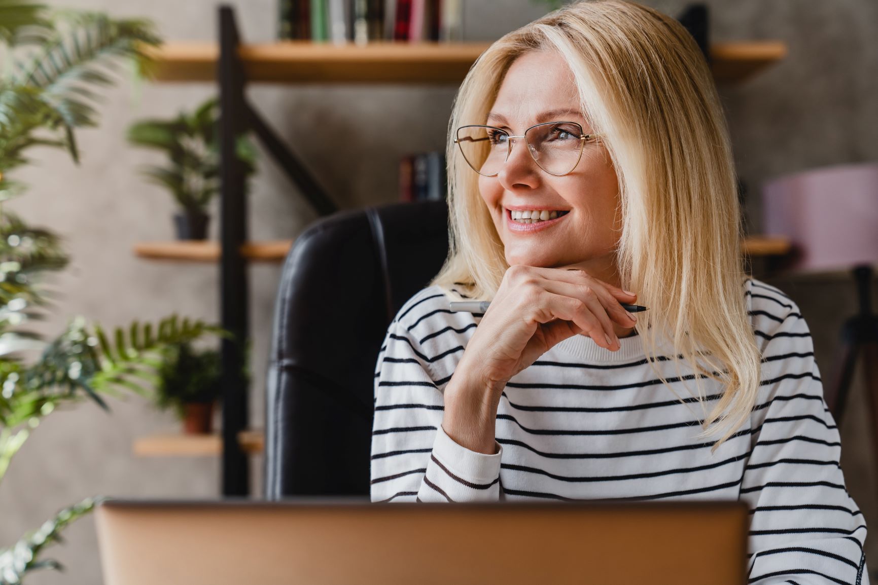 Blonde woman with shoulder-length hair and glasses in white & black striped shirt at comptuer dreaming manifestation for beginners, manifesting your dream life