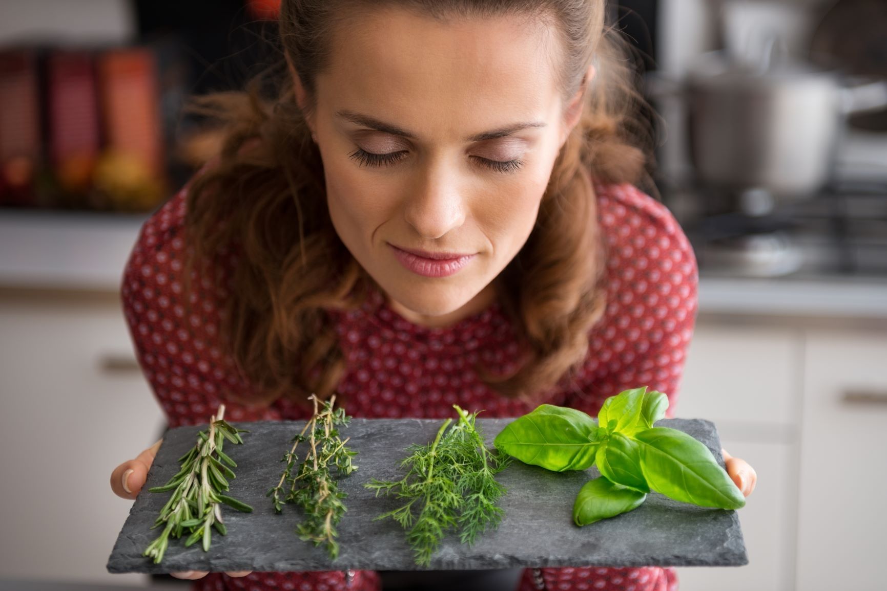 Supercharge your metabolism Brown haired woman in red polk dot blouse leaning over slate cutting board with herbs