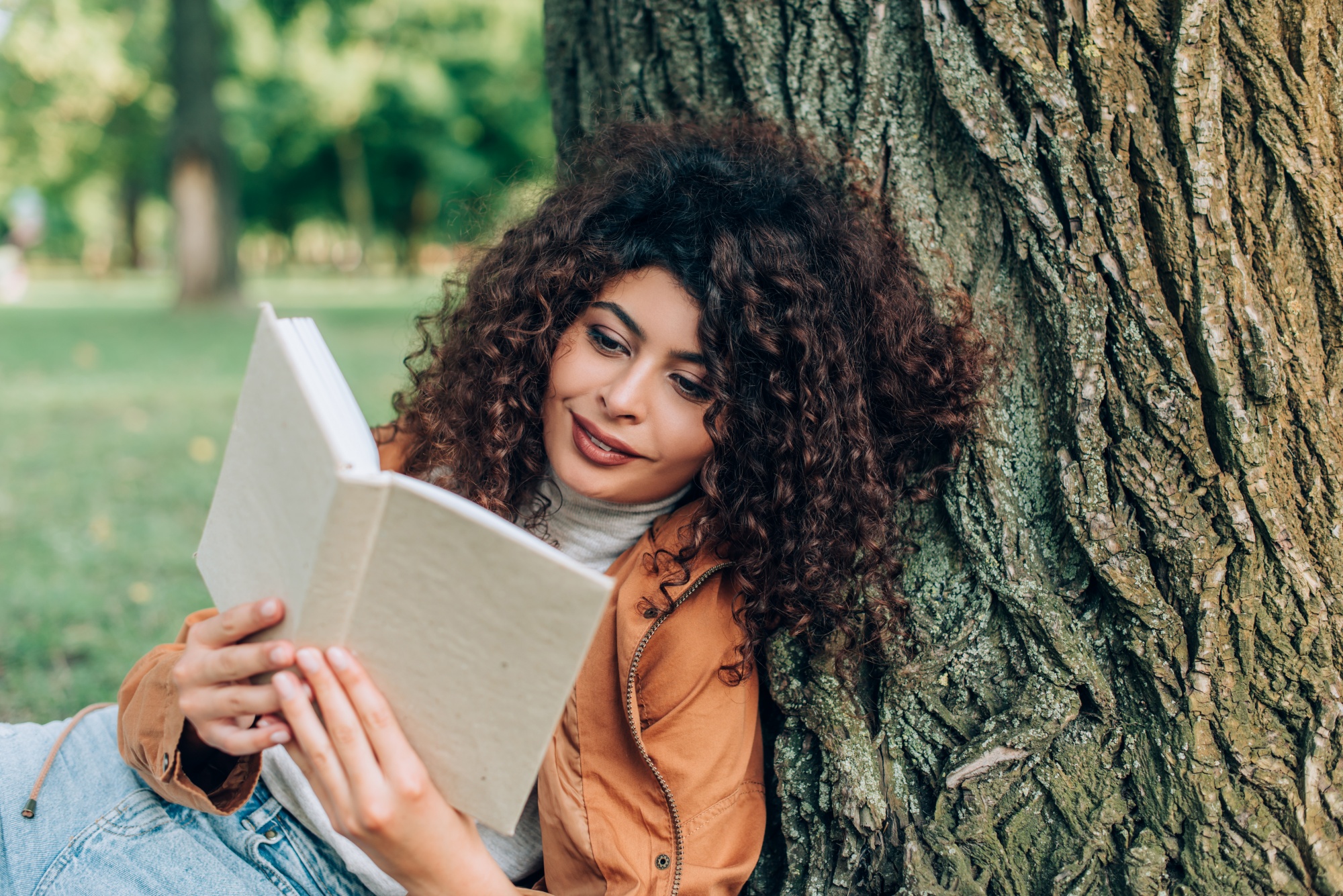 why reinventing yourself makes you younger, Curly woman reading book near tree in park
