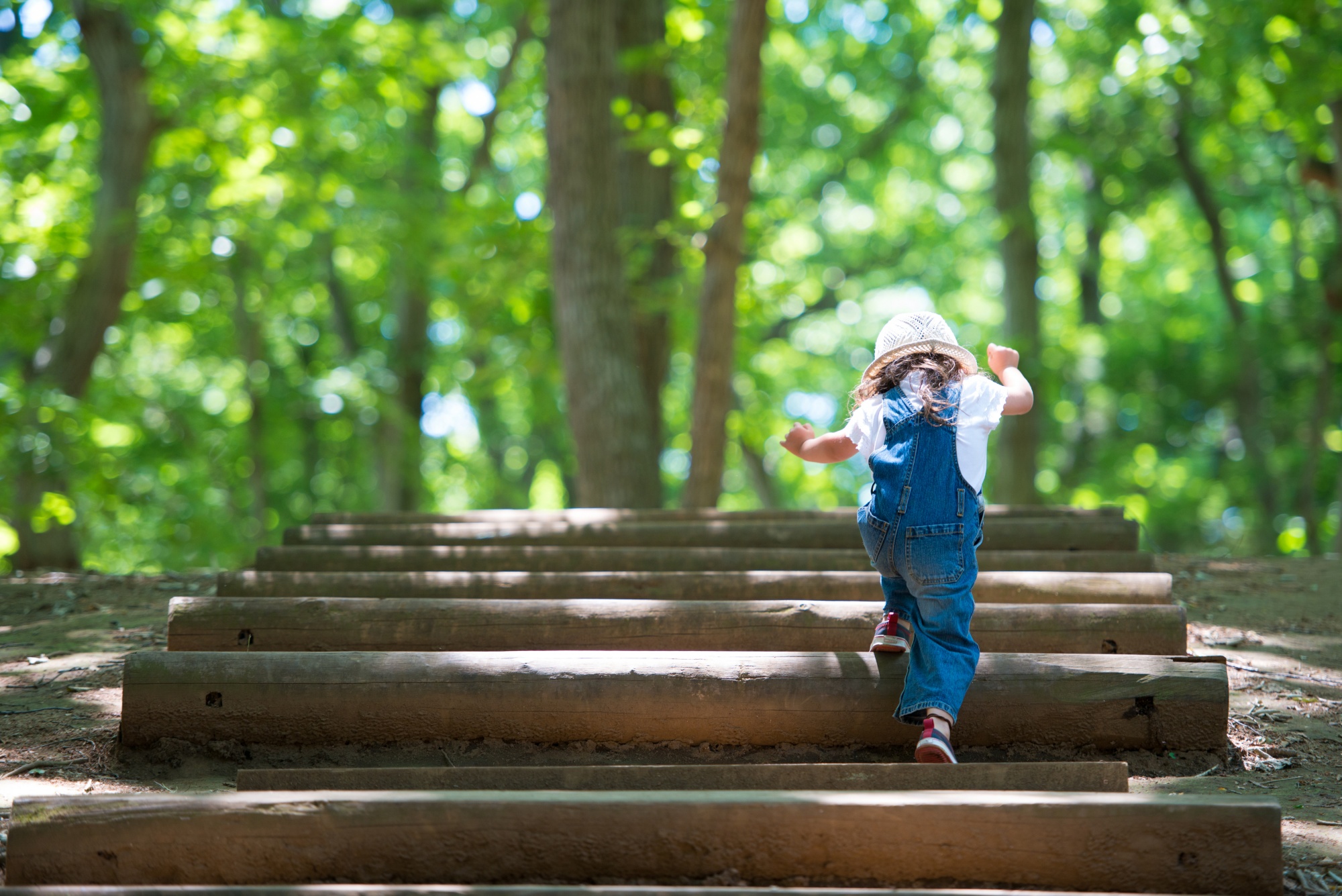 why reinventing yourself makes you younger, Little Girl in denim overalls and pink hat climbing steps in the woods