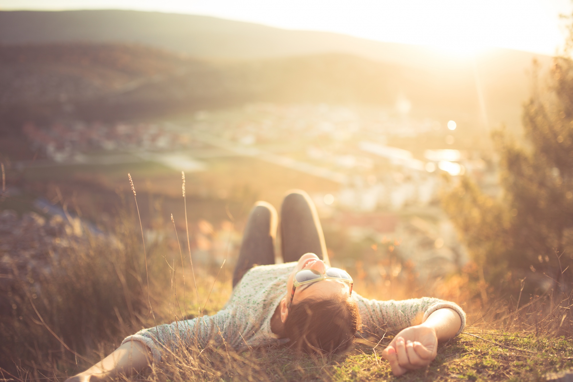 Woman laying on grass on hill above a town manifestation for beginners, manifesting your dream life