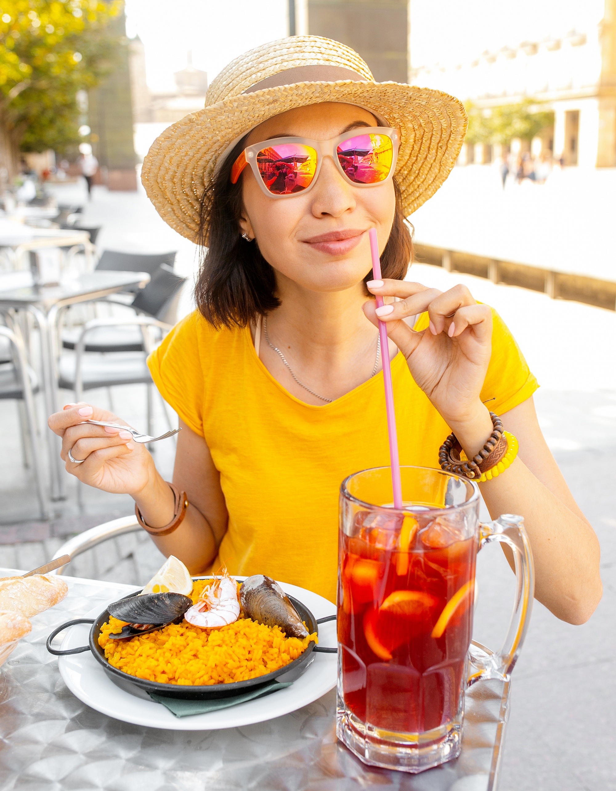 travel destinations for foodies, woman over 40 in sunglasses eating Paella and sangria fruit wine outdoors on a sunny day