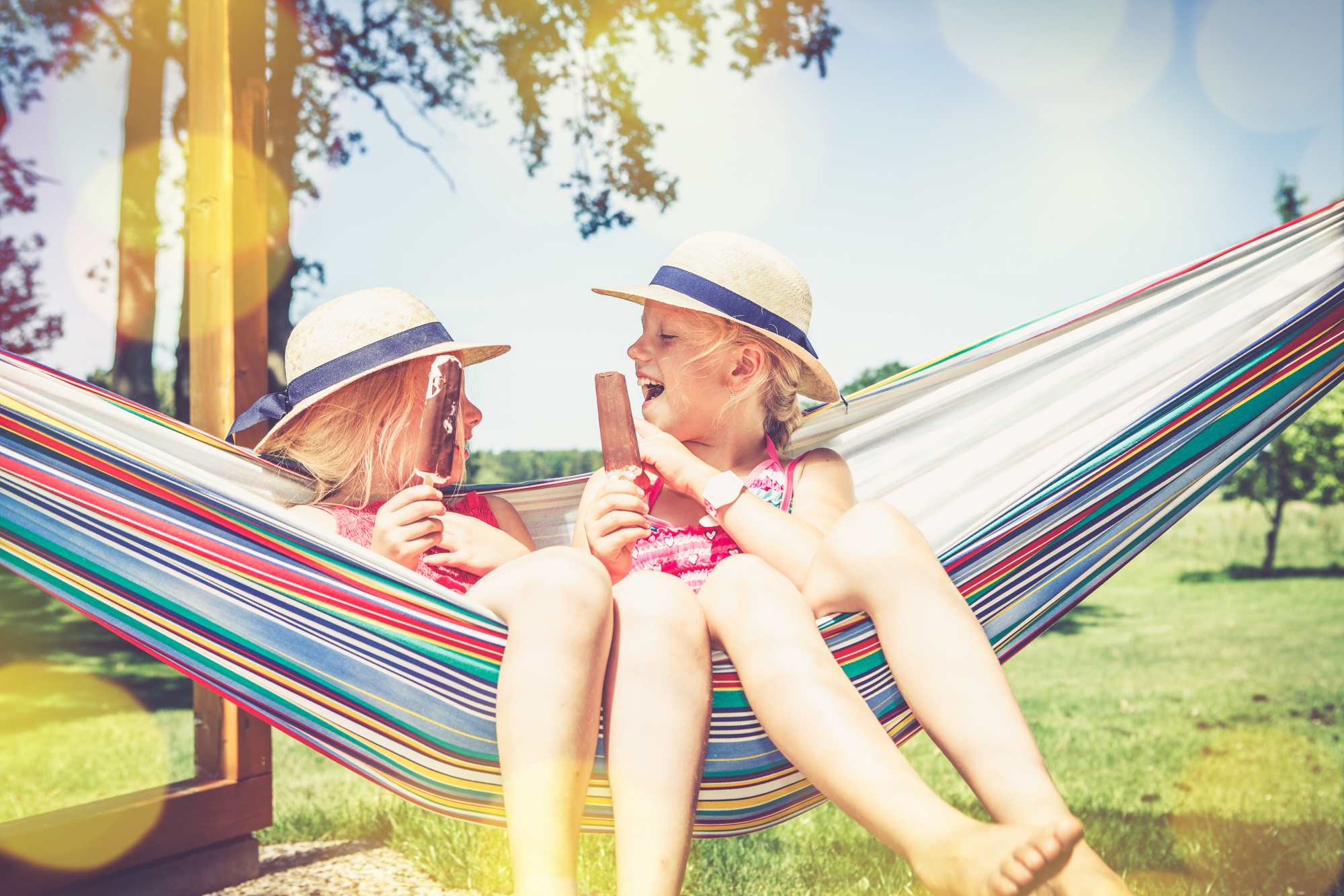 Essentials to Get Your Kids Outdoors, two young girl friends sitting outdoors in a hammock laughing eating ice cream in the summer sun
