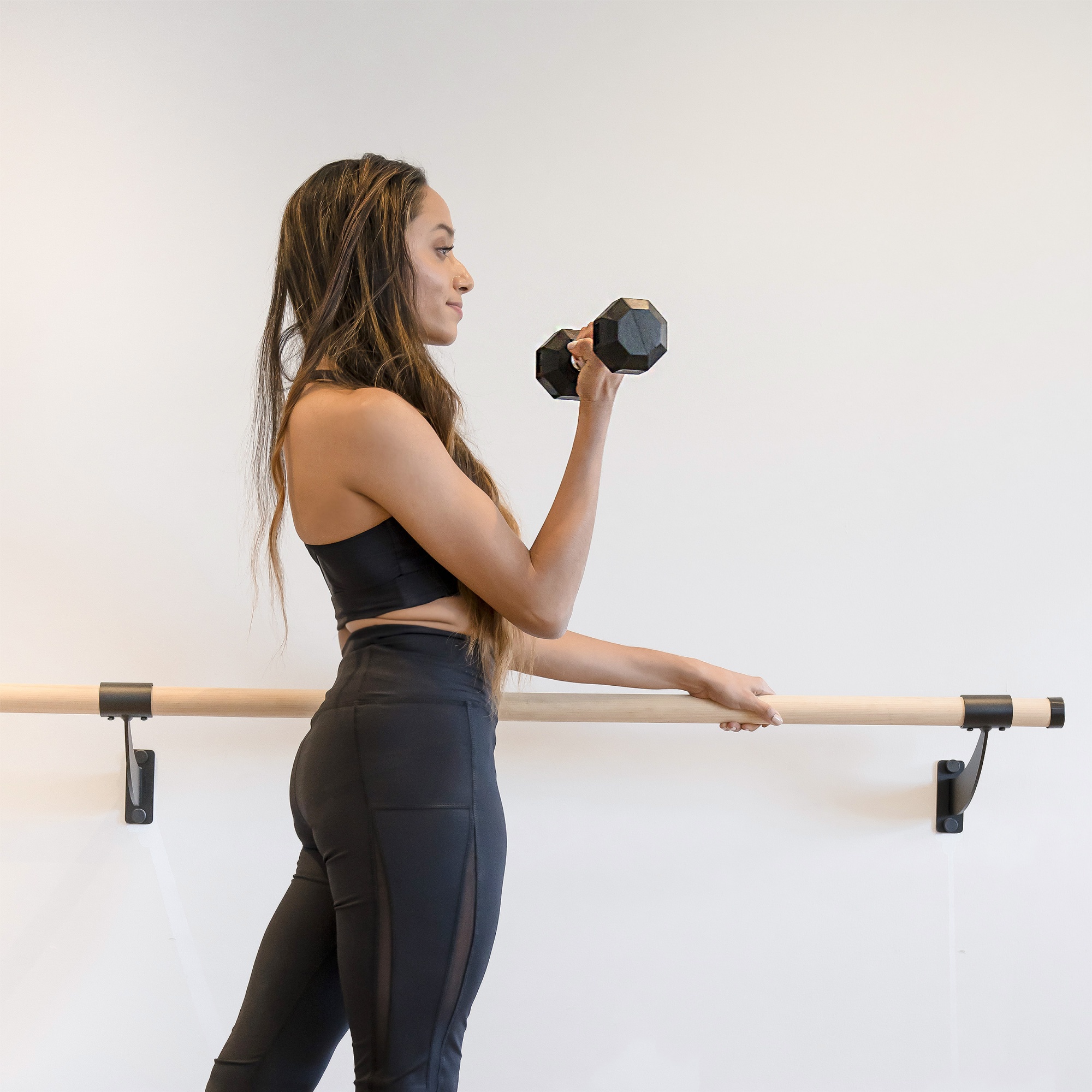 how to get rid of flabby arms, Black woman in black leggings at barre with dumbbell