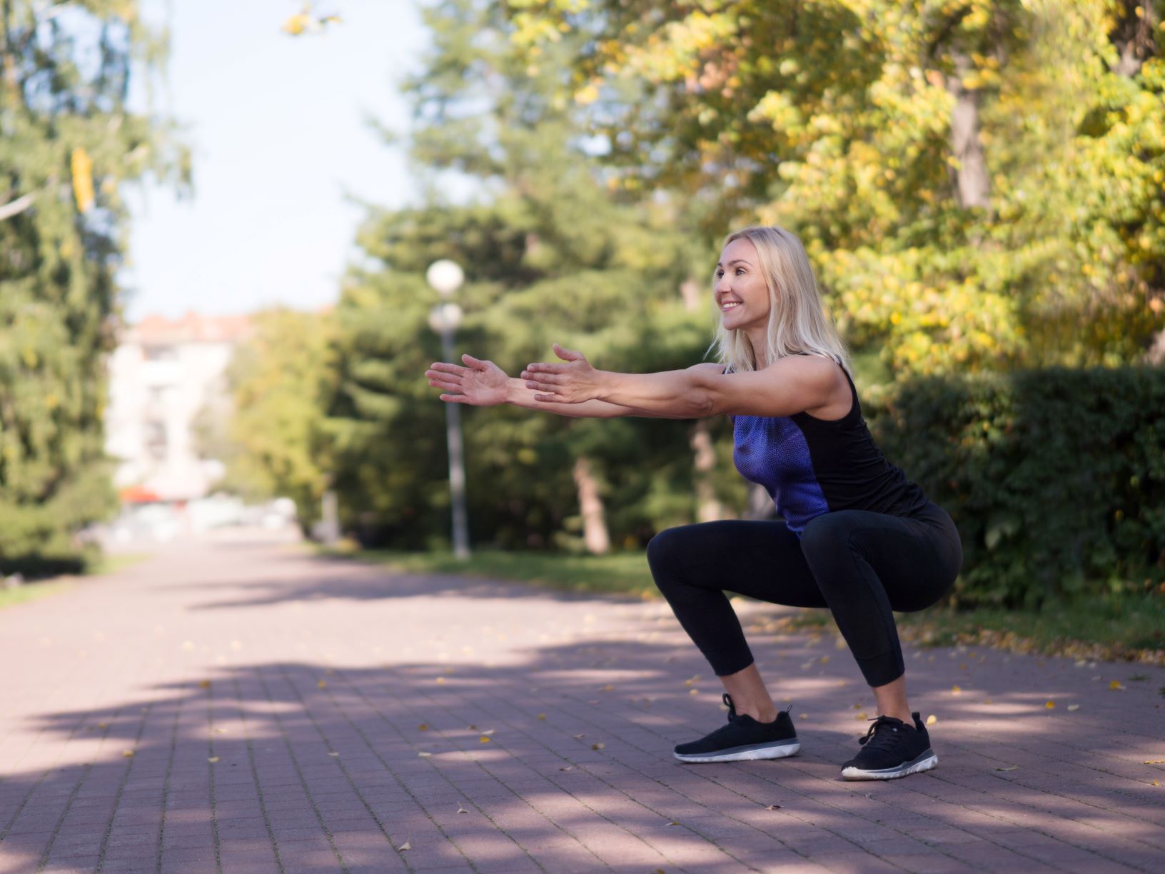 Middle-aged woman outside in deep squat, workouts to get your booty swimsuit ready