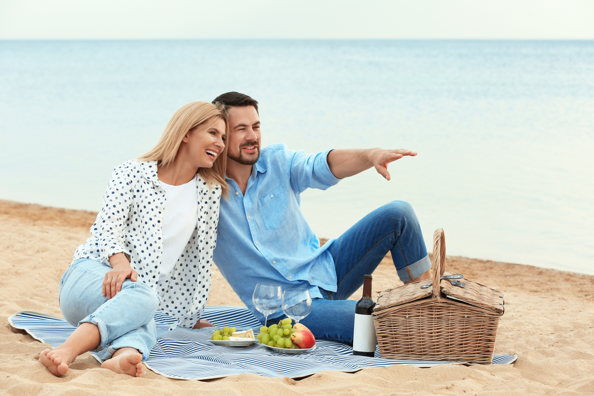 romantic picnic for two, couple sitting on picnic blanket at the beach