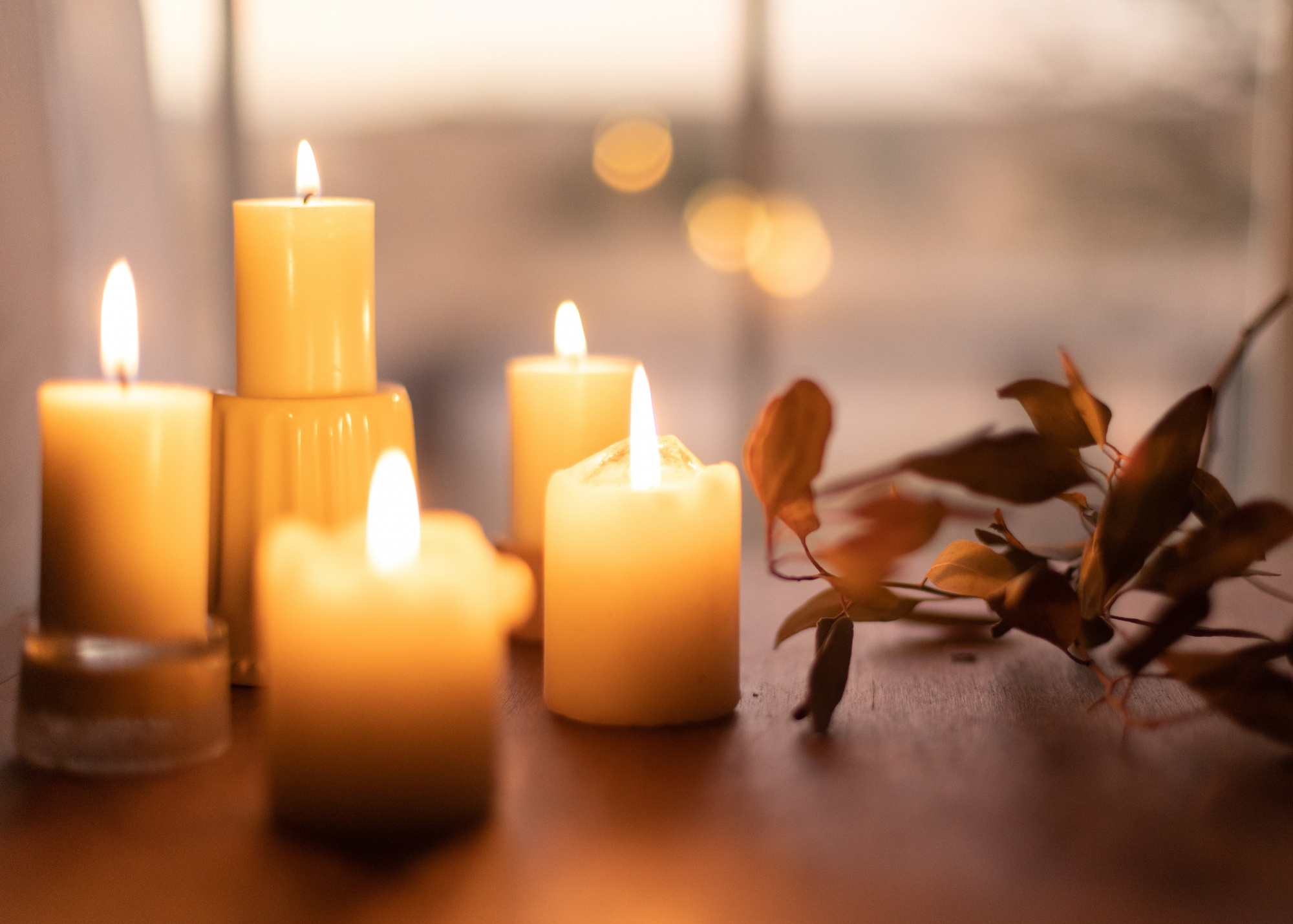 fall-scented candles, home décor with lit candles and leaves on a wooden table 