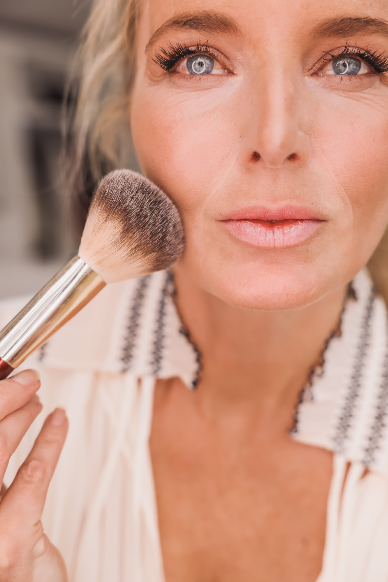 woman using a face brush one of the makeup brushes you need