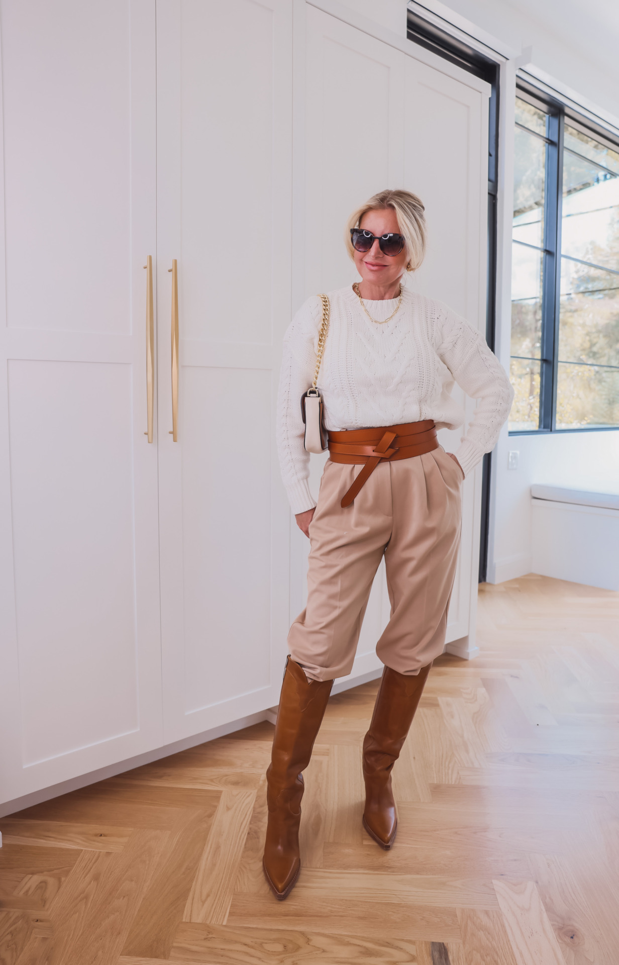 how to wear pleated pants, ways to wear pleated pants, ways to style pleated pants, how to style pleated pants, pleated trousers women, pleated pants over 40, favorite daughter pleated pants, pleated pants 2023, pleated pants outfits, erin busbee, busbee style, fashion over 40, pistola white cable knit sweater, paris texas knee high brown boots, le spec sunglasses, marc jacobs tri-color handbag, isabel marant obi belt
